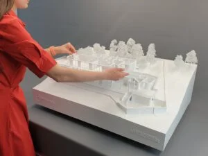Architekturmodell einer modernen weißen Villa mit abnehmbaren Ebenen; Person platziert ein Geschoss auf dem Geländemodell.