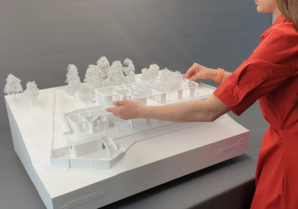 Architekturmodell einer modernen weißen Villa mit abnehmbaren Ebenen; Person platziert ein Geschoss auf dem Geländemodell.