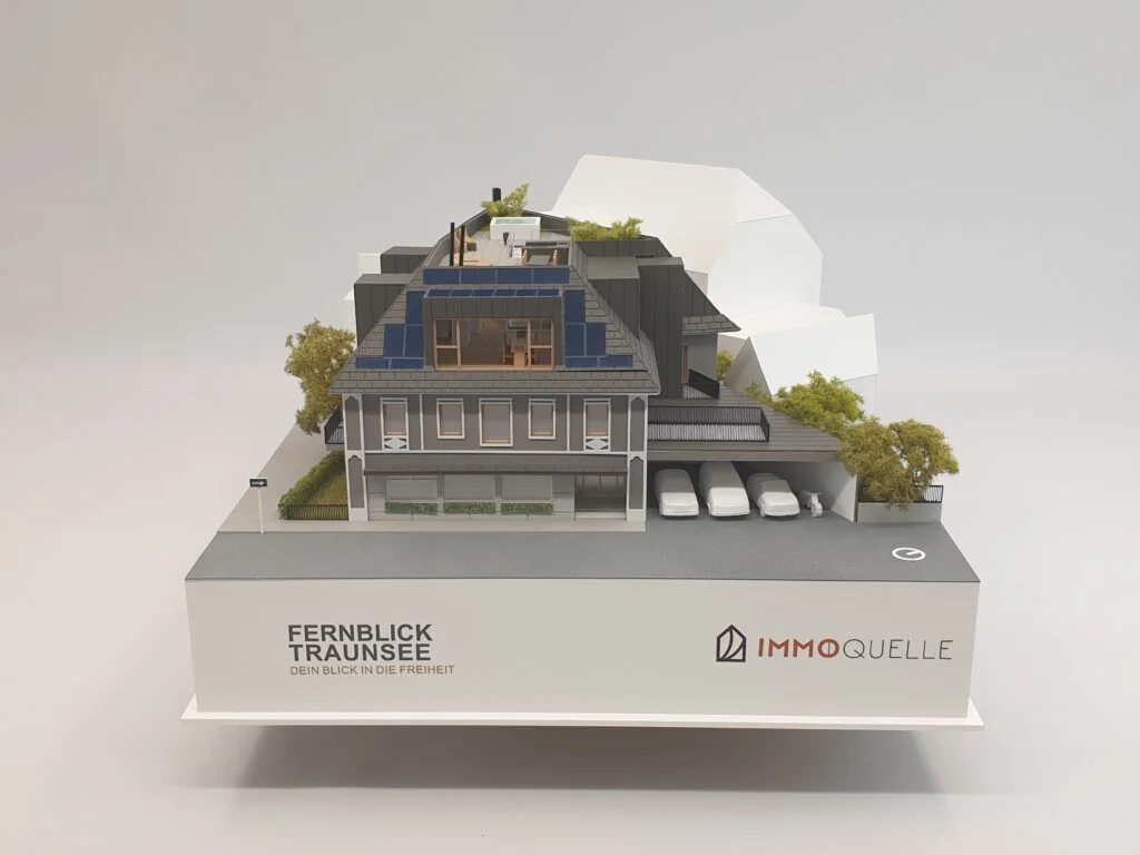 Architekturmodell auf weißem Podest mit Logo Fernblick Traunsee und Immoquelle, Vorderansicht mit Carports und Gebäudestruktur.