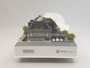 Architekturmodell auf weißem Podest mit Logo Fernblick Traunsee und Immoquelle, Vorderansicht mit Carports und Gebäudestruktur.