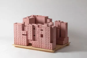 Massives rosa Ausstellungsmodell auf Holzpodest mit monolithischem Baukörper und tiefen Fassadenaussparungen.