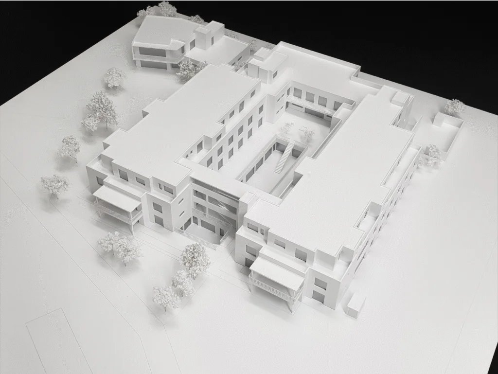 Weißes Architekturmodell einer mehrgeschossigen Wohnanlage mit Innenhof und umliegenden Bäumen im Maßstab.