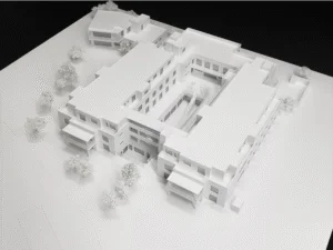 Weißes Architekturmodell einer mehrgeschossigen Wohnanlage mit Innenhof und umliegenden Bäumen im Maßstab.