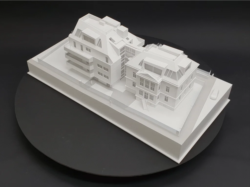 Weißes Architekturmodell mit modernem Neubau und historischem Gebäude, Seitenansicht auf einem schwarzen Drehteller.