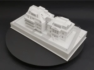 Weißes Architekturmodell mit modernem Neubau und historischem Gebäude, Seitenansicht auf einem schwarzen Drehteller.