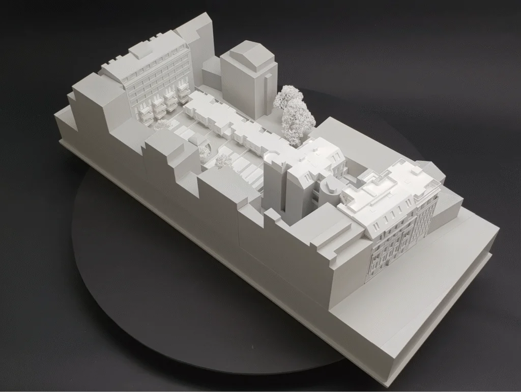Weißes Ausstellungsmodell eines urbanen Blockensembles mit Innenhof, Baumgruppen und detaillierter Dachstruktur in Aufsicht.
