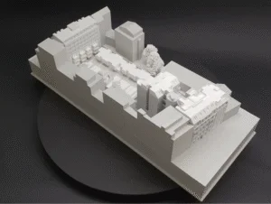 Weißes Ausstellungsmodell eines urbanen Blockensembles mit Innenhof, Baumgruppen und detaillierter Dachstruktur in Aufsicht.