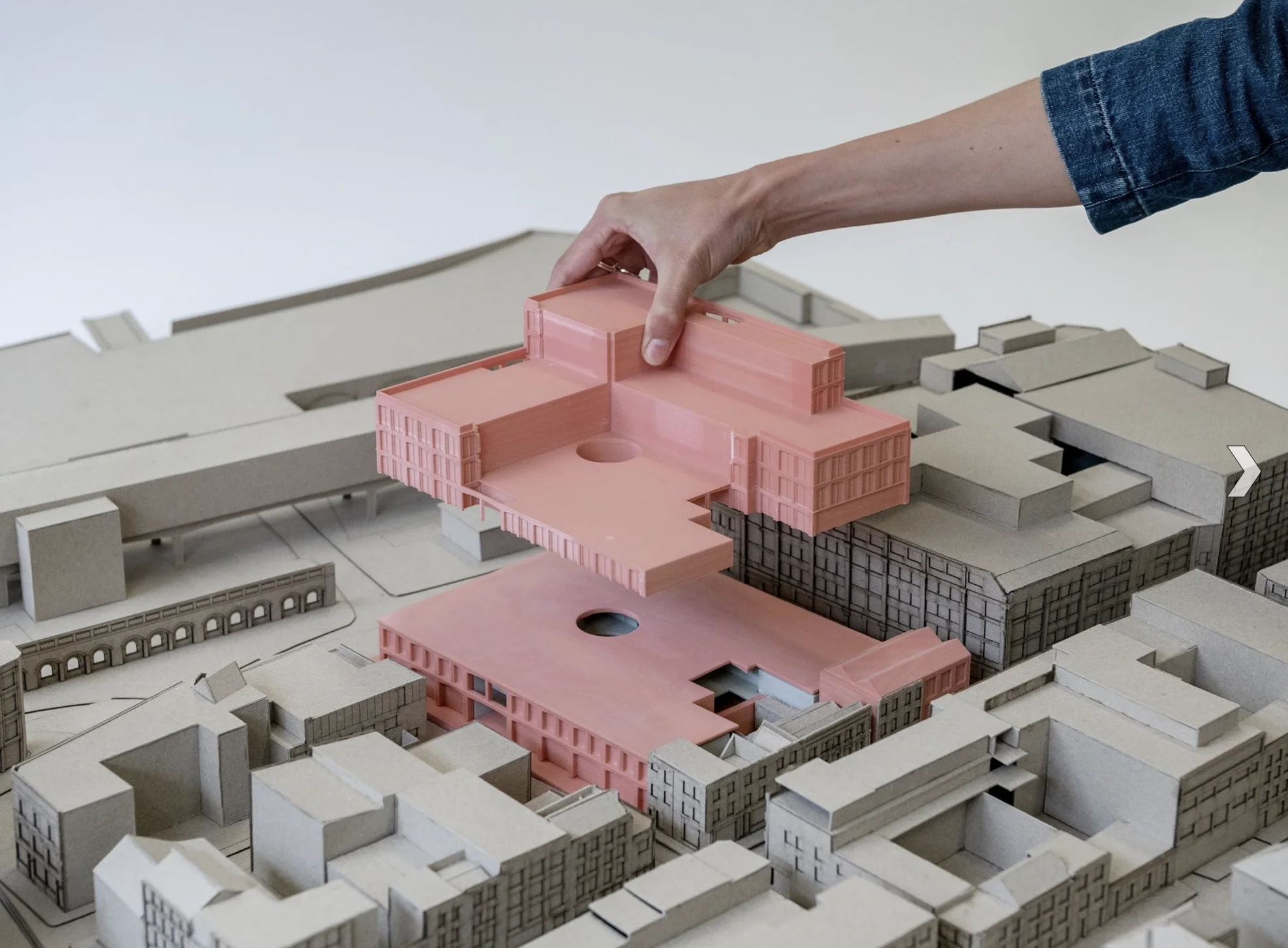 Hand platziert ein herausnehmbares Gebäudeteil in ein graues städtebauliches Ausstellungsmodell mit präzisen Blockstrukturen.
