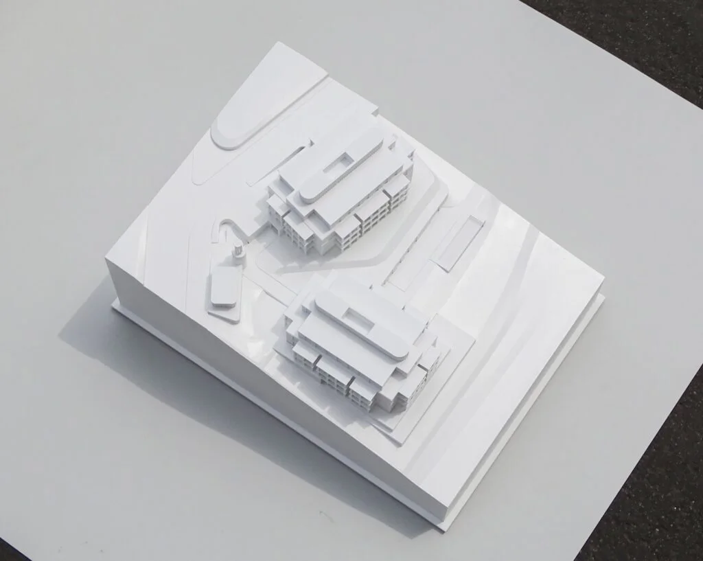Weißes Architekturmodell mit zwei modernen Gebäuden auf schrägem Gelände und klaren Volumenstudien im Maßstab 1:200.
