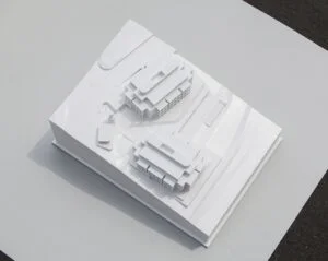 Weißes Architekturmodell mit zwei modernen Gebäuden auf schrägem Gelände und klaren Volumenstudien im Maßstab 1:200.