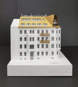 Architekturmodell eines sanierten Gründerzeitgebäudes mit goldfarbenem Dachausbau und Balkonen