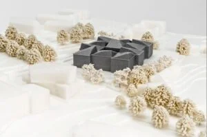 Dunkler Gebäudekörper als Fokus in einem weißen Landschaftsmodell mit umliegenden Volumen und modellierten Bäumen.