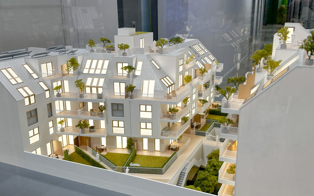 Architekturmodell mit beleuchteten Wohnungen, Terrassen und begrünten Dachflächen in detaillierter Ausführung.
