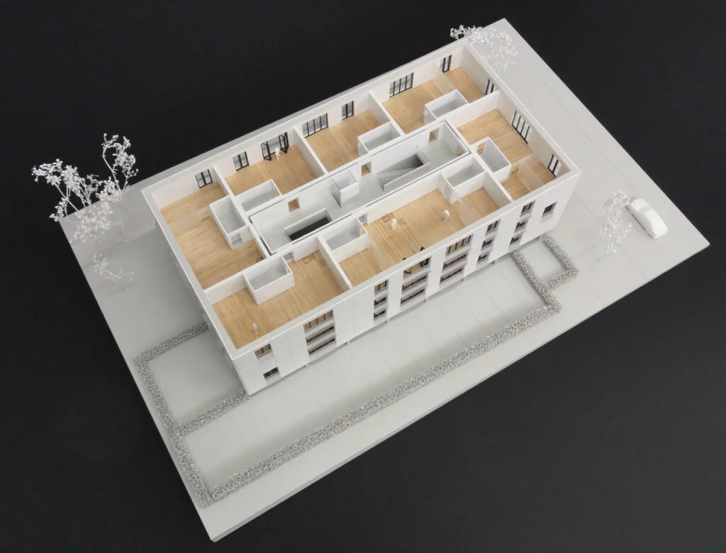 Weißes Architekturmodell eines Wohngebäudes mit offenem Innenraum und detaillierten Grundrissen im Maßstab 1:200.
