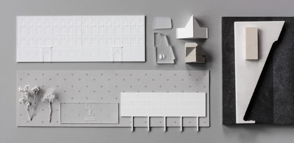 Flach angeordnete Materialien und Bauteile für ein Architekturmodell mit Fassadenteilen, Bäumen, Sockelplatten und Kleinteilen.