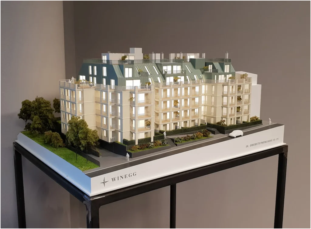 Architekturmodell eines hochwertigen Wohnensembles mit begrünten Außenflächen, Balkonen und ausgebauter Dachlandschaft.