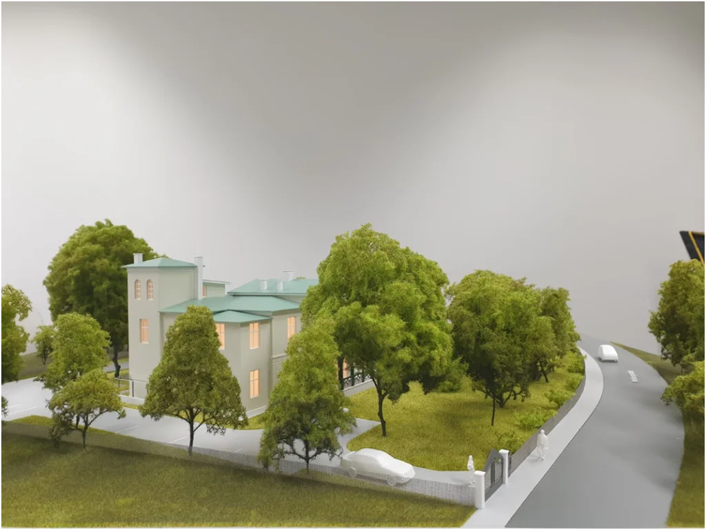 Architekturmodell eines freistehenden Wohngebäudes in grüner Umgebung mit Bäumen und Erschließungsstraße.