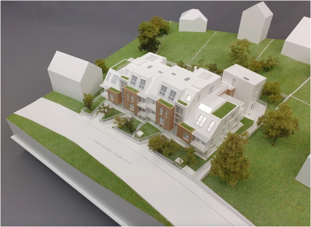 Weiẞes Architekturmodell mit grünen Wiesen und Bäumen – Wohnbauprojekt im Maßstab 1:100