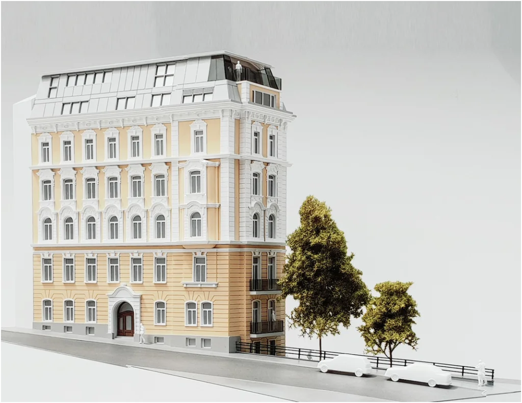 Detailliertes Immobilienmodell im Maßstab 1:100 eines klassischen Zinshauses mit modernem Dachgeschossausbau und Fassadenschmuck