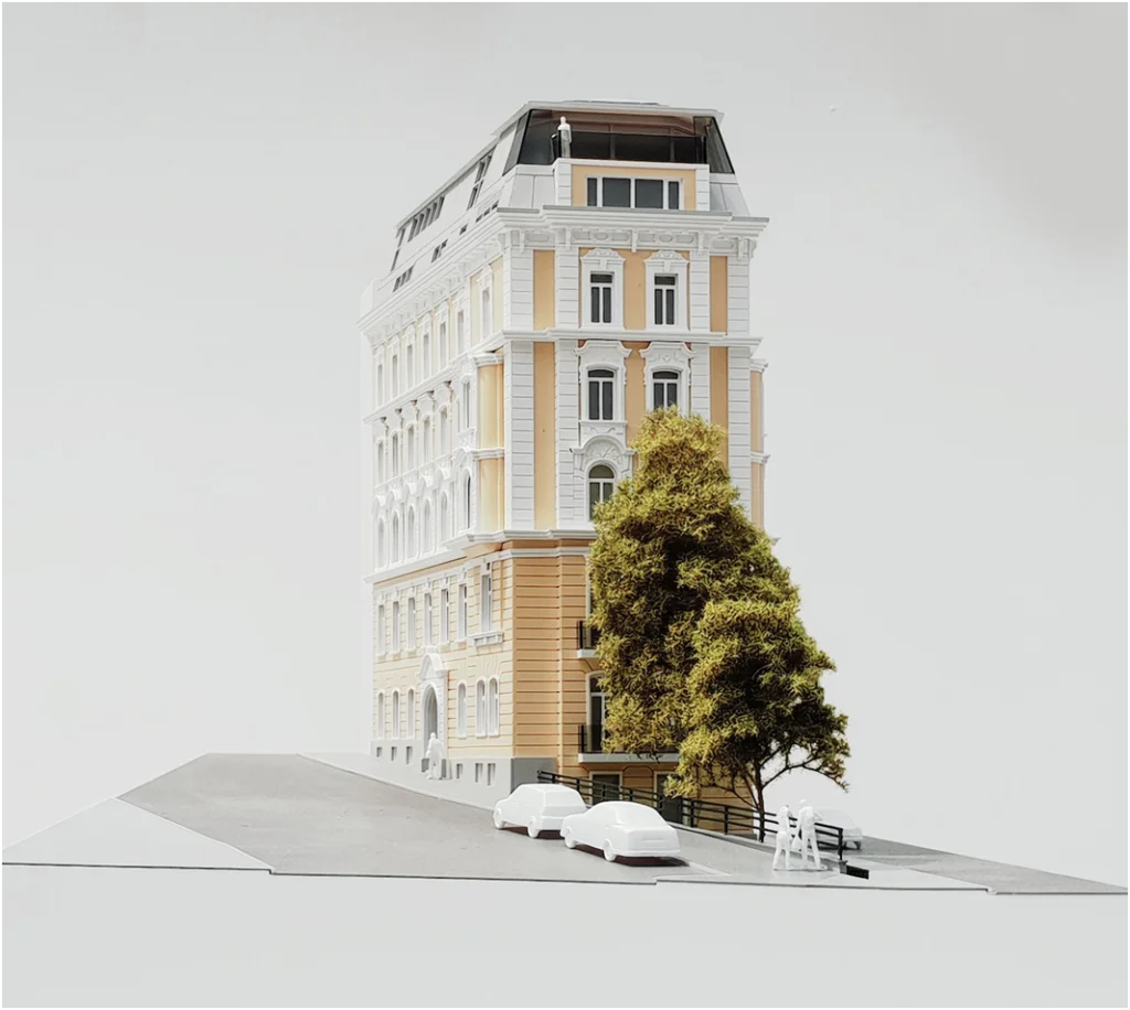 Perspektivansicht eines Immobilienmodells im Maßstab 1:100 zeigt ein sanierte Zinshaus mit modernem Dachausbau und Straßendetails