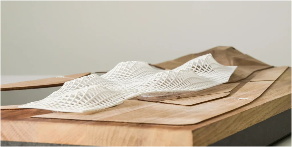 Detailansicht eines Architekturmodells aus Holz mit geschwungener, filigraner Gitterstruktur auf topografischer Oberfläche