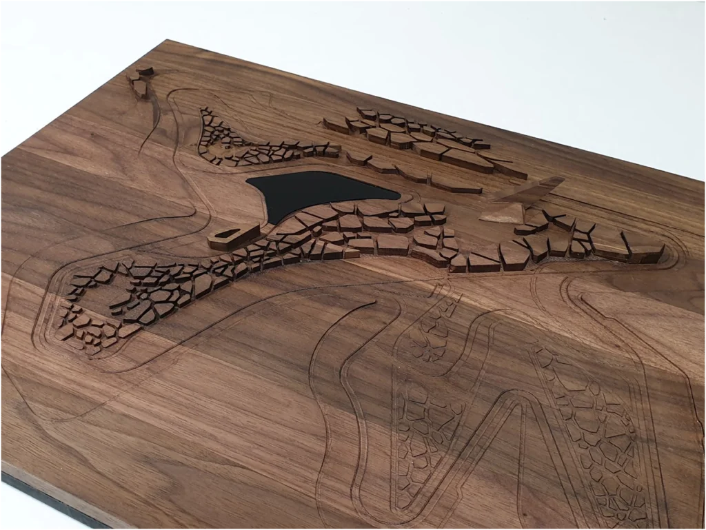 Topografisches Architekturmodell aus Holz mit gelaserten Geländelinien, fragmentierter Bebauungsstruktur und integriertem Wasserbecken