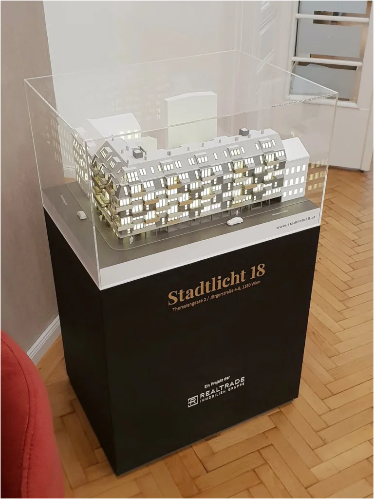 Exklusives Präsentationspodest mit Firmenlogo – Individuelle Farbe nach Wahl und Vor-Ort-Montage Schwarzes, foliertes Modellpodest aus MDF mit goldenem Projektlogo und aufgebautem Architekturmodell vor Ort