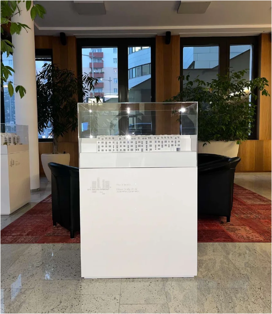 Modellpodest in Weiß nach Wahl – Maßgeschneidert für Bauträger Weißes Modellpodest aus folierten Platten mit dezentem Firmenlogo präsentiert in einem modernen Verkaufsrau