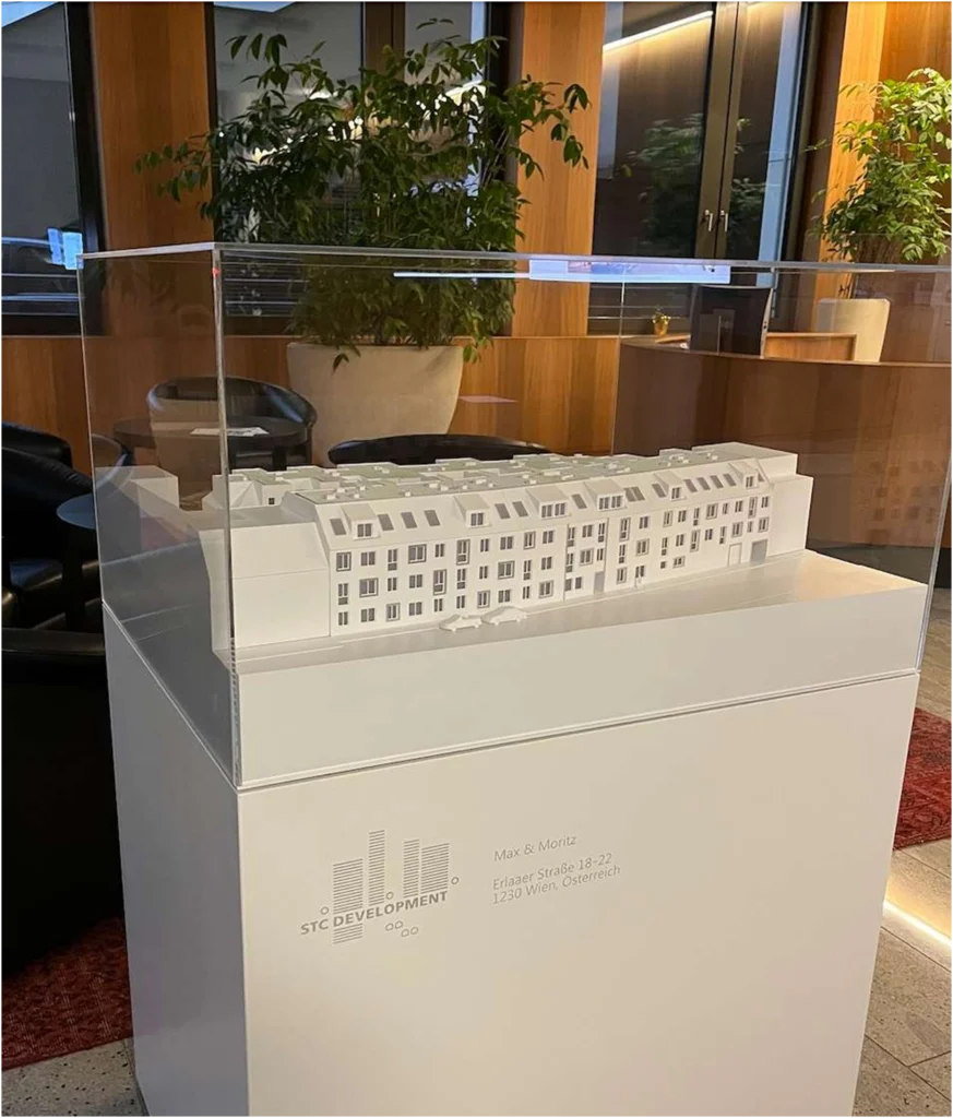 Minimalistisches Modellpodest in Weiß – Maßgefertigt aus MDF-Platten Weißes foliertes Podest für Architekturmodelle mit dezentem Firmenlogo der STC Development in einem modernen Verkaufsraum