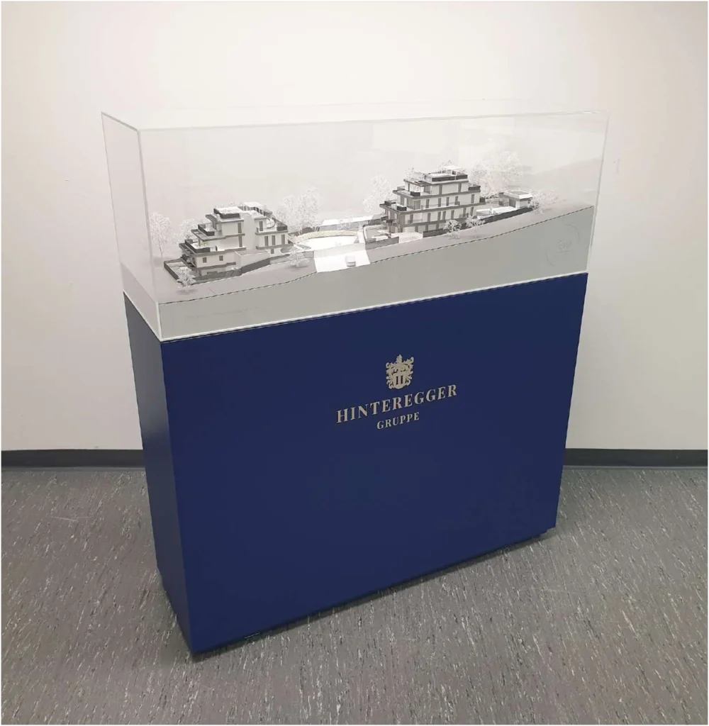 Farbiges Podest für Architekturmodelle – Individuelle Folierung Dunkelblaues Modellpodest mit silberner Logo-Prägung für eine hochwertige Markenpräsentation vor Ort