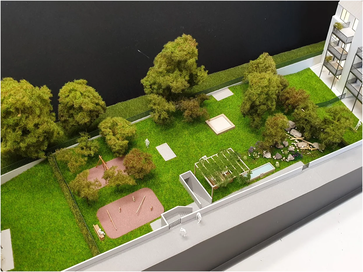 Architekturmodell mit Freiraumgestaltung, Grünflächen, Spiel- und Aufenthaltsbereichen sowie dichter Bepflanzung, vollfarbige Darstellung eines Wohninnenhofs