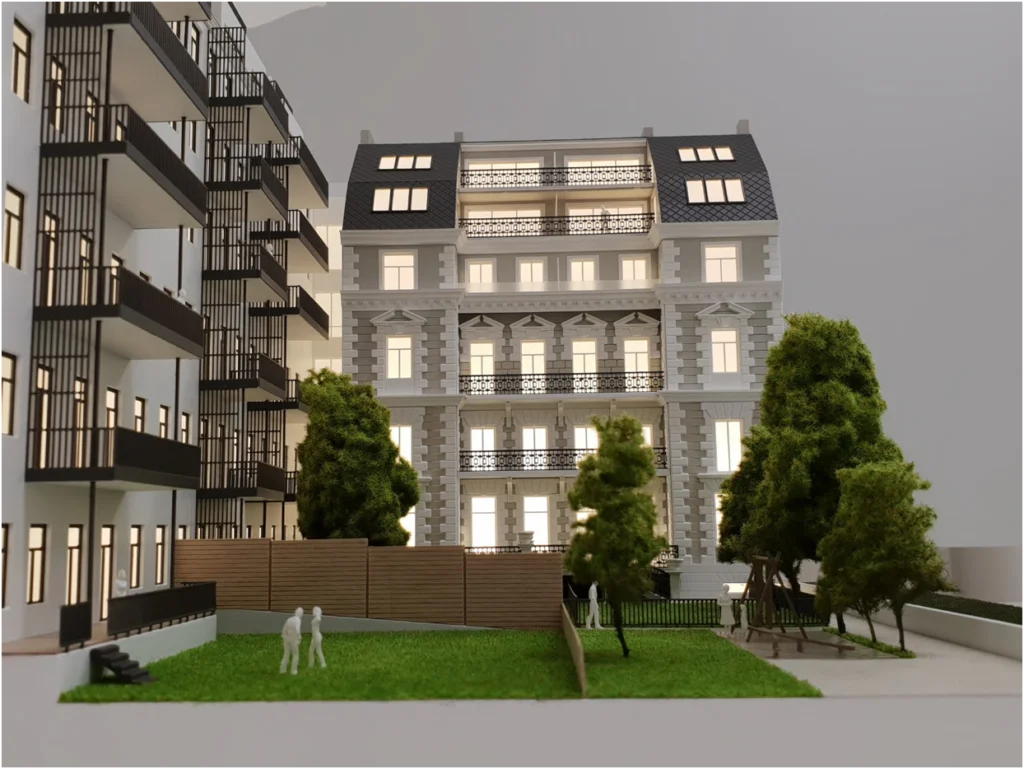 Architekturmodell eines Altbau-Wohngebäudes mit Innenhof, begrünten Freiflächen und angrenzendem Neubau.