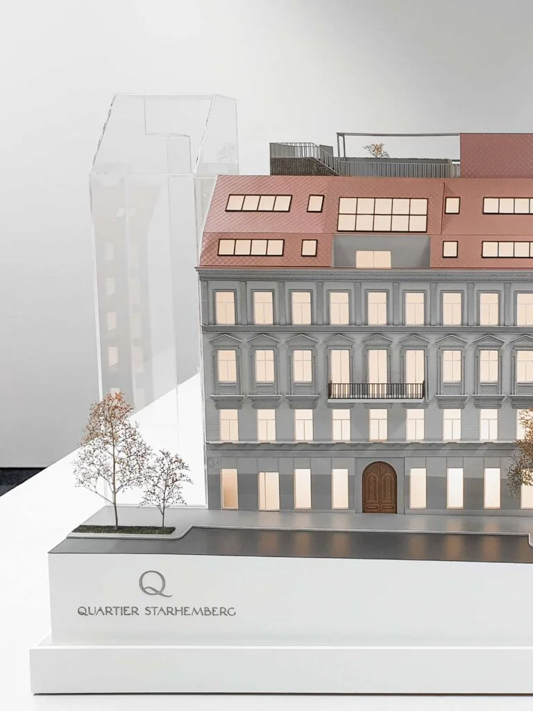 Architekturmodell Quartier Starhemberg: Vollfarbige Fassade mit Mansarddach, beleuchteten Fenstern und Umgebungsmodell.