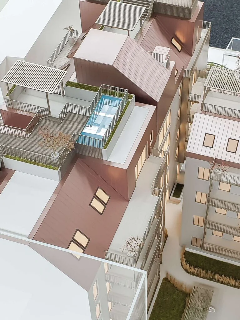 Vollfarbiges Architekturmodell 1:75: Detaillierte Fassade mit Mansarddach, beleuchteten Fenstern und Logo-Präsentation.